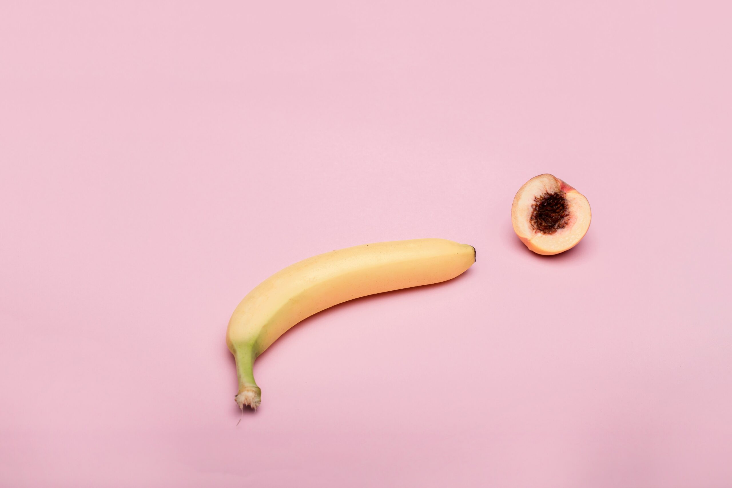 banana and half a peach on a light pink background