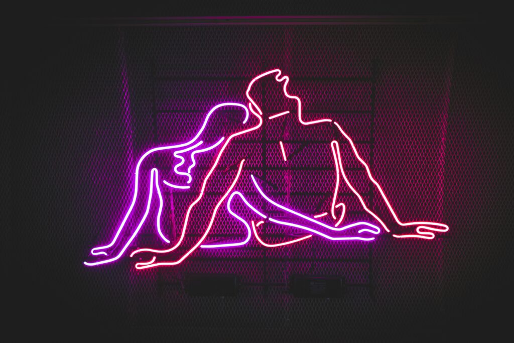 man and woman lined drawing in pink and red neon on black background