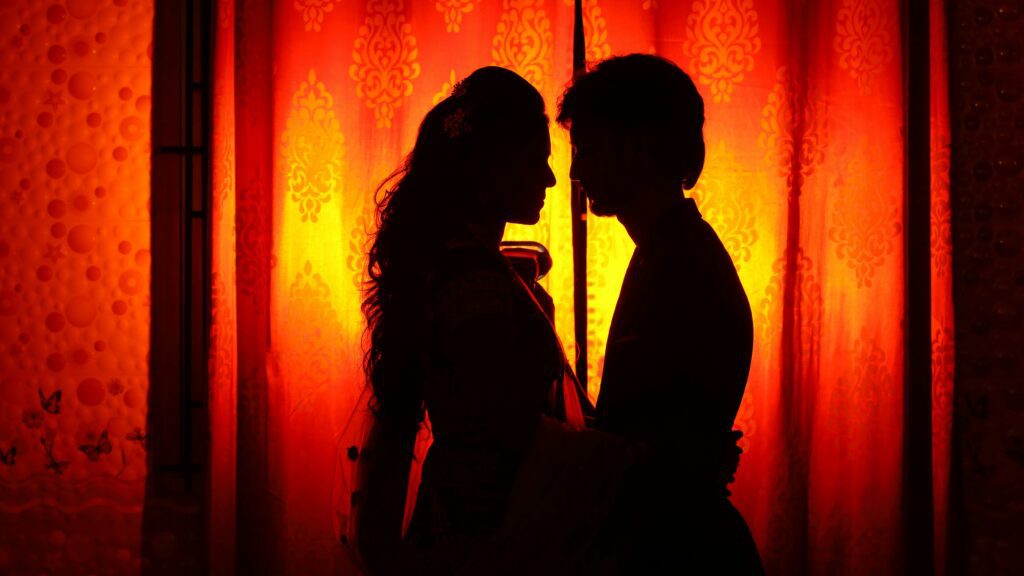 man and woman in silhouette kissing with red background