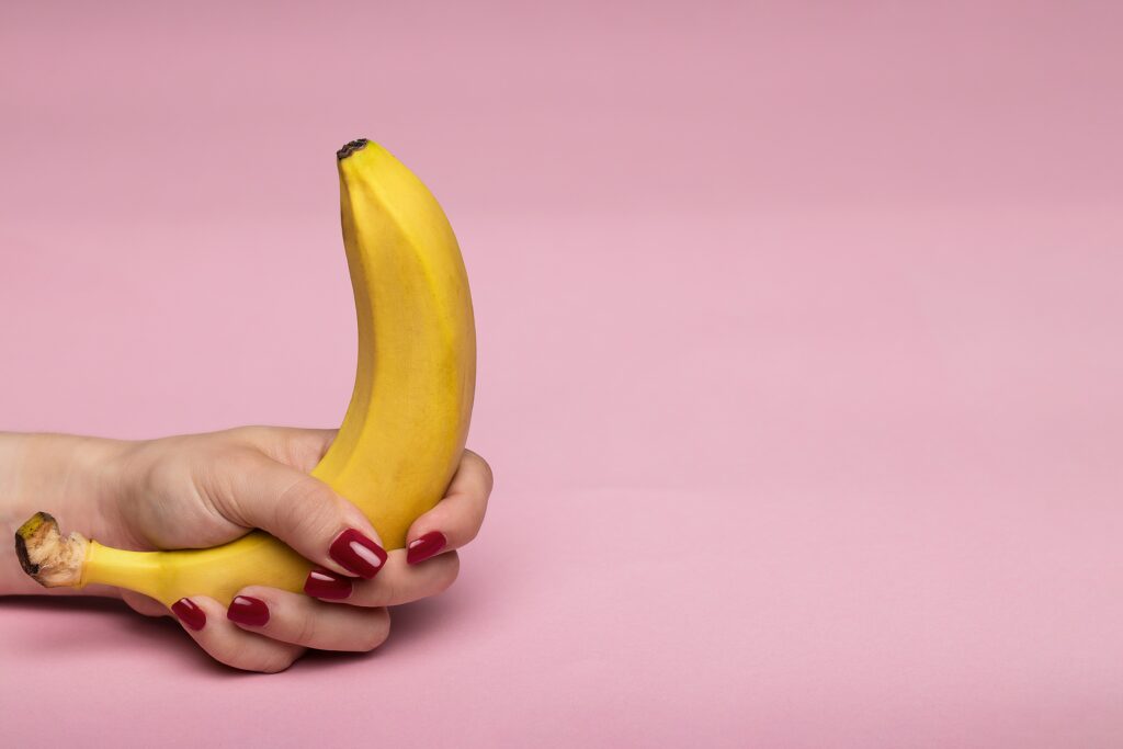 woman holding a banana with a pink background