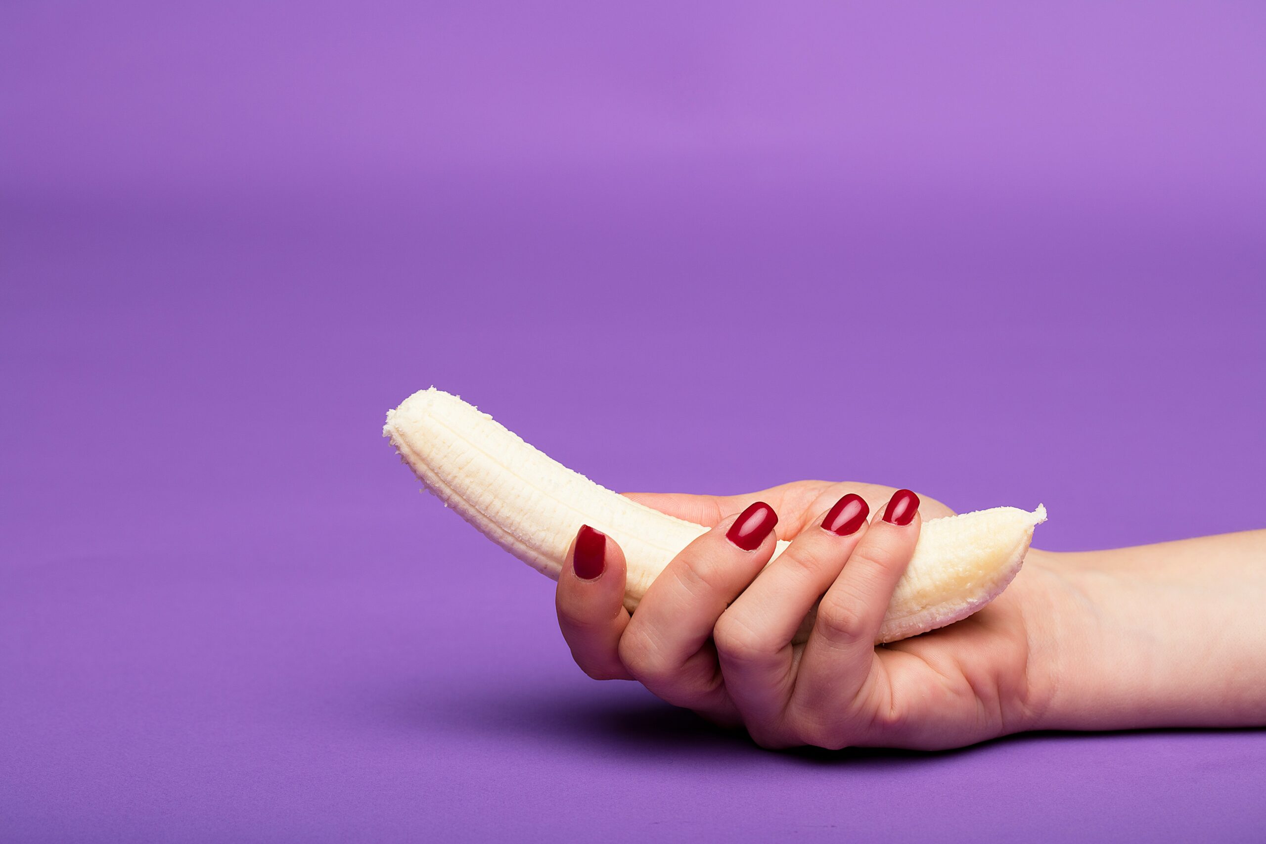 woman holding an unpeeled banana with purple background