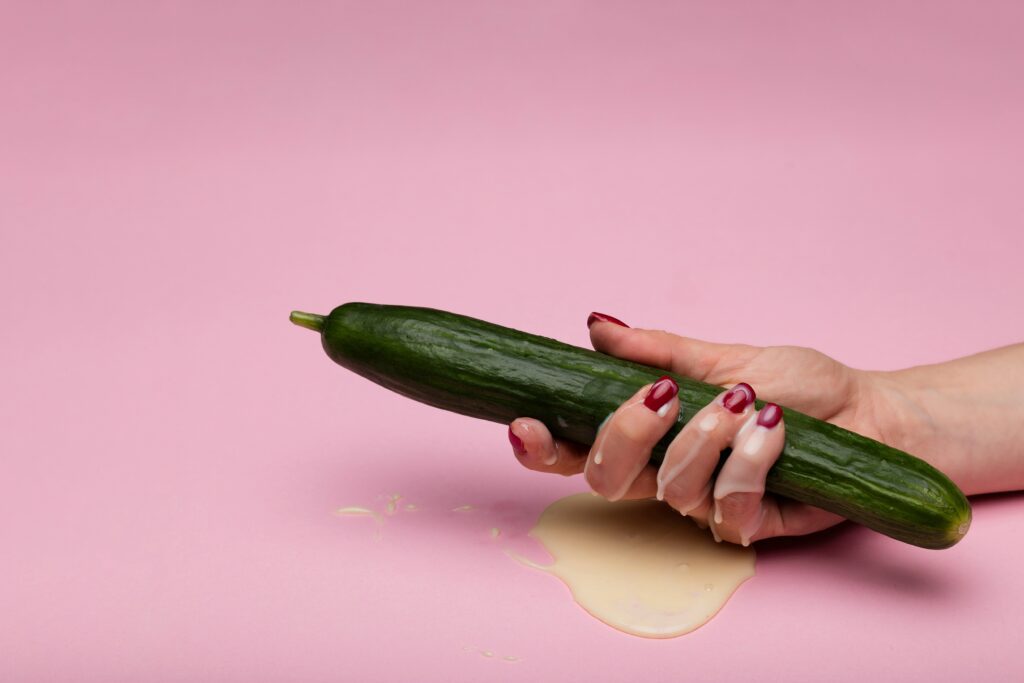 woman's hand holding cucumber on a pink background