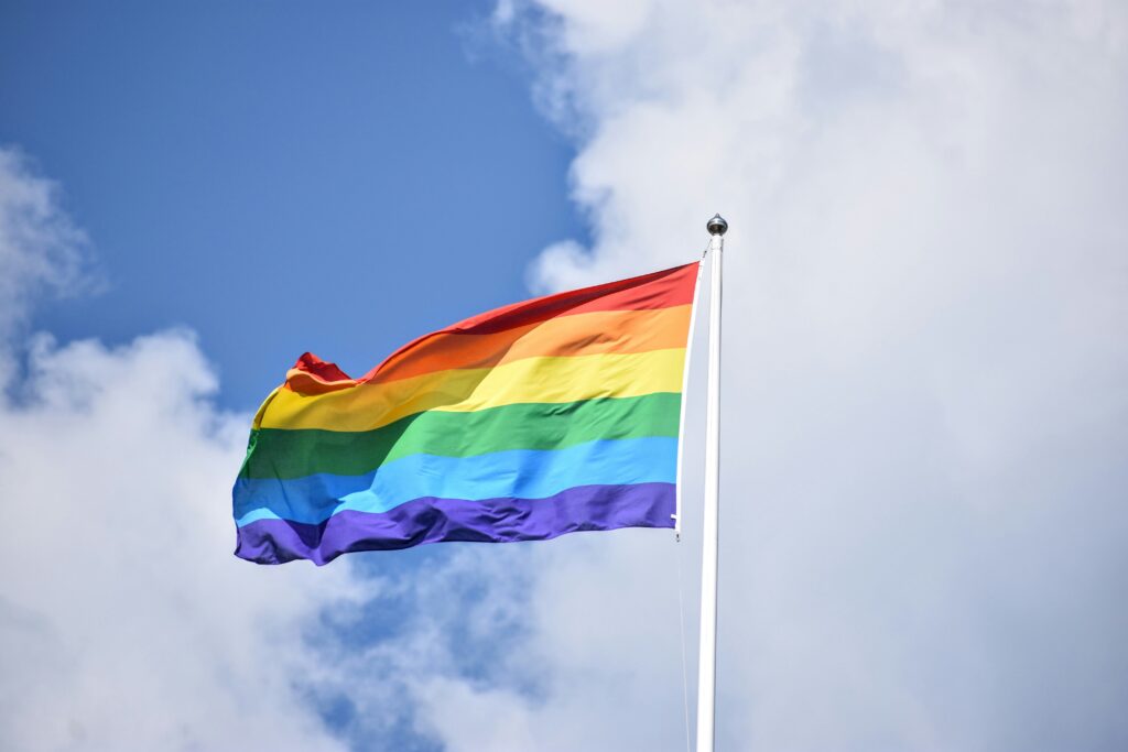 Rainbow pride flag against blue sky with clouds