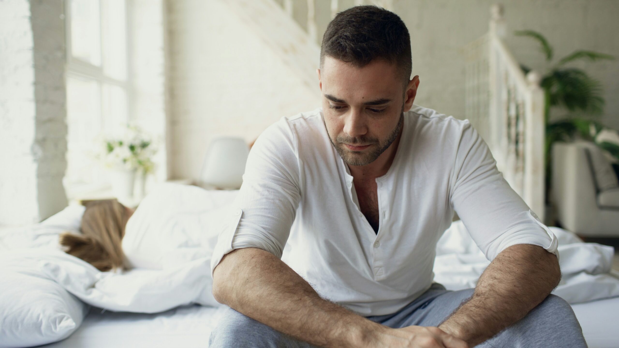 sad man on bed while girlfriend sleeps