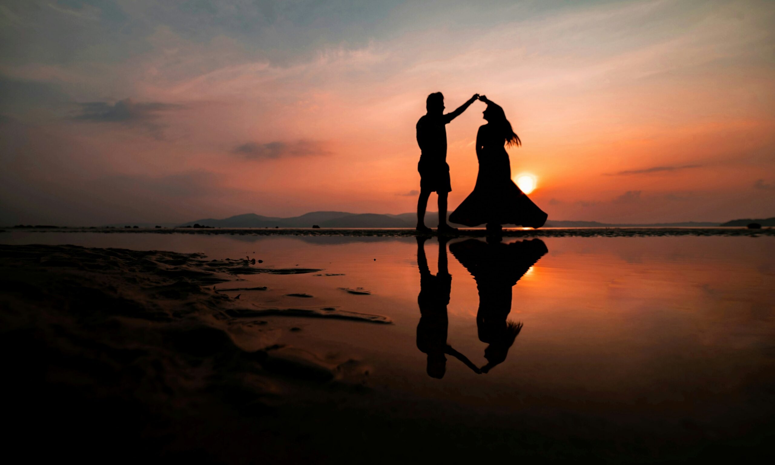 Man and woman dancing on the beach at sunset